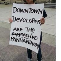 Sign being held outside reading Downtown developers are the aggressive panhandlers