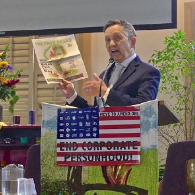 Dennis Kucinich, 60-ish white guy in a suit at a podium holding up a copy of the Free Press