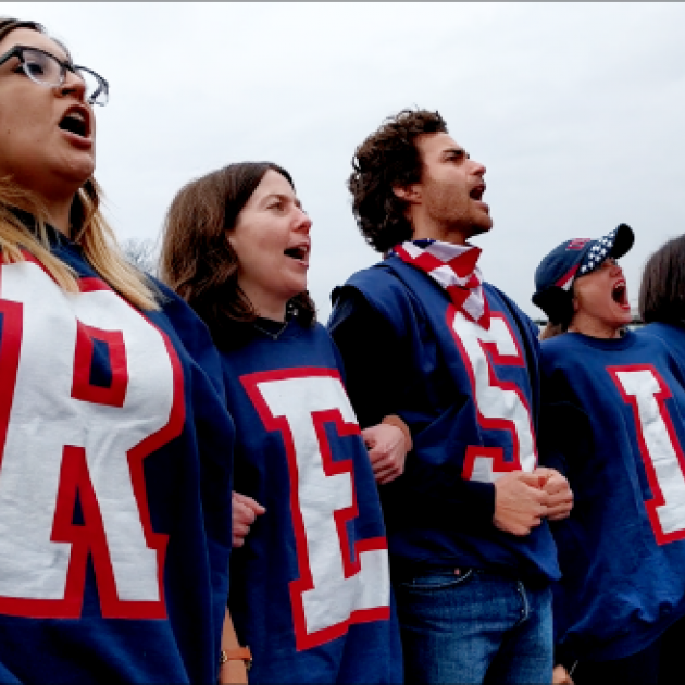 People dressed in red, white and blue with RESIST spelled out on each shirt yelliing