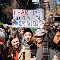 Young people wearing winter coats one young man holding a sign above his head that says Fear has no place in our schools