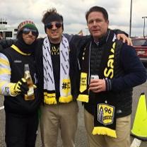 Three white guys wearing Save the Crew clothes smiling at the camera posing with their arms around each other