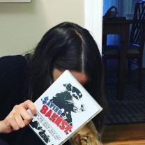 Women with dark hair leaning over hiding her face with a book, Saving Banksy