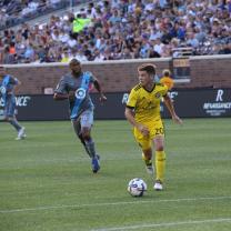 Two soccar players on the field on opposite teams, one in blue and one in yellow kicking the ball