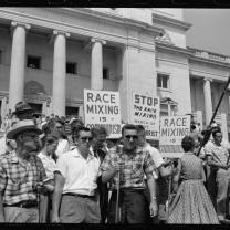 Black and white photo of protest in streets from 50s with sign saying something about race mixing