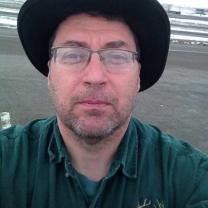 Man with glasses and wide brimmed black hat, looking grim