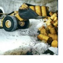 Bulldozer pushing yellow barrels into a ditch