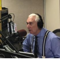 Gray haired white man in blue shirt wearing headphones talking into an elaborate microphone set up